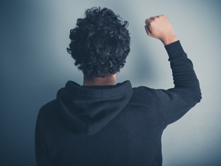 Rear view shot of a young man in a hooded top raising his fist in the airの写真素材