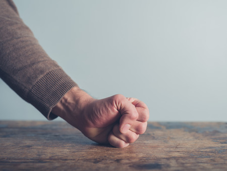 Closeup on a man slamming his fist on a wooden tableの写真素材