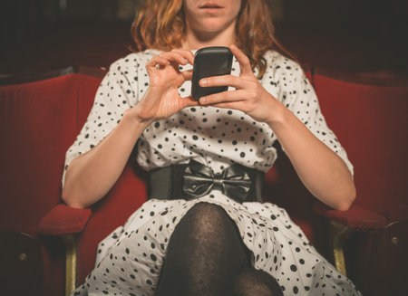 A young woman is sitting on the front row in a movie theater and is using her phone