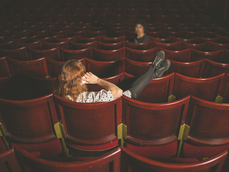 A young woman is talking on her phone in an auditorium and is annoying a man a few rows in front of herの写真素材