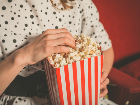 Closeup on a young woman eating popcorn in a movie theaterの写真素材