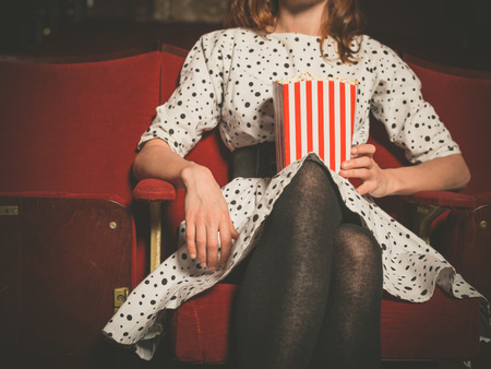 A young woman is sitting in a movie theater with a bucket of popcornの写真素材