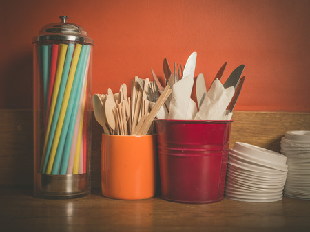 A selection of cutlery, colorful straws and plastic lids for disposable cups on a wooden tableの写真素材