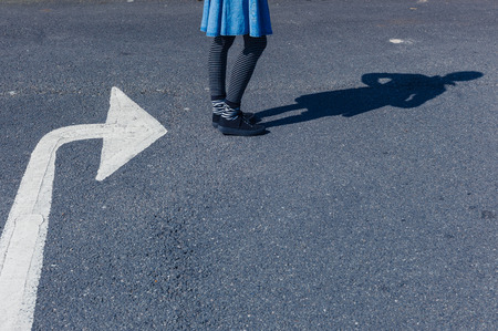 A young woman is standing outside in the street and is facing the direction a big arrow painted on the road is pointingの写真素材