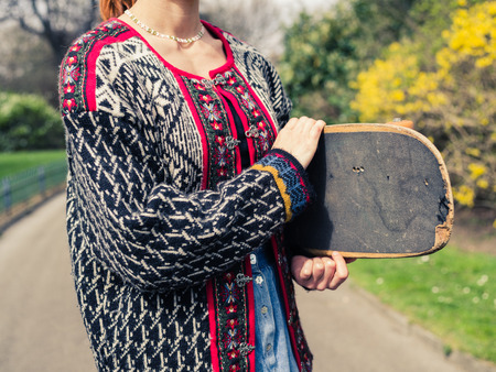 A young woman is walking in the park on a spring day with her skateboard under her armの写真素材