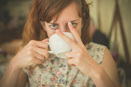 A young woman is drinking coffee and is displaying an obscene gesture with her fingersの写真素材