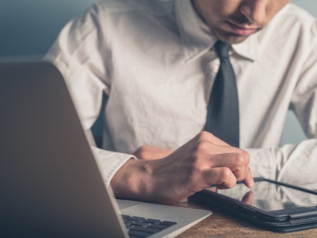 A young businessman is using a tablet while typing on a laptop computerの写真素材