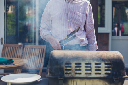 A senior man is attending to a barbecue in the garden on a sunny dayの写真素材