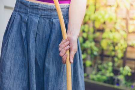 A young woman is standing outside in a garden and is holding a hoseの写真素材