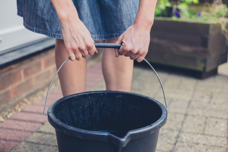 A young woman is lifting a big bucket outside in a gardenの写真素材