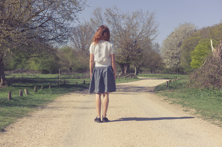 A young woman is standing on a dirt road in a forestの写真素材