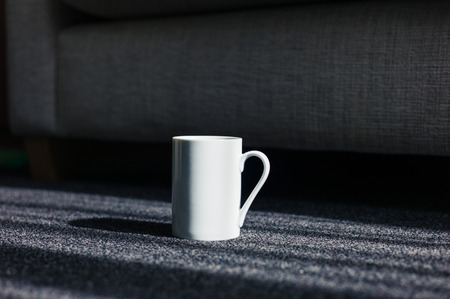 A white mug on a carpet  by a sofa at homeの写真素材