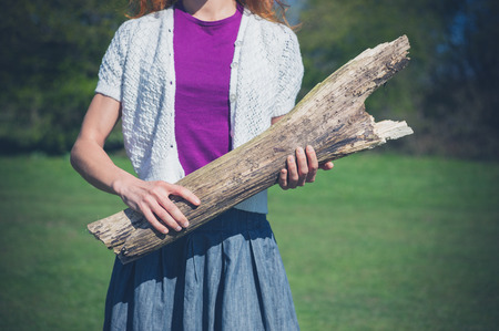 A young woman is standing on the grass in a clearing of a forest and is holding a large logの写真素材