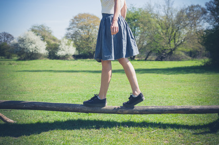 A young woman is walking in the forest and is balancing on a wooden beamの写真素材