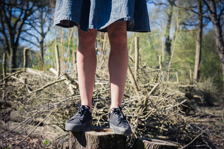 A young woman wearing a blue skirt is standing on a tree trunk in the forest on a sunny spring dayの写真素材
