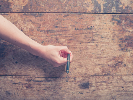 A female hand is writing on a wooden desk with a penの写真素材