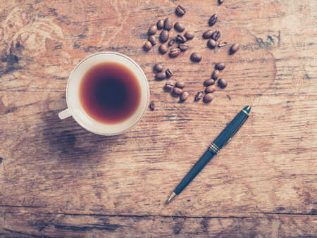 A cup of coffee with beans and a pen on a wooden tableの写真素材
