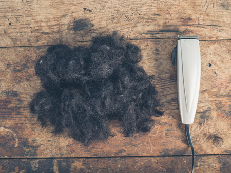A large pile of cut hair and some clippers on a wooden tableの写真素材