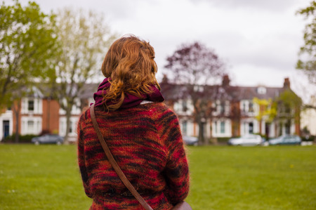 A young woman is walking in a park with some terraced houses in the backgroundの写真素材