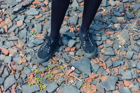 The feet and legs of a young woman standing on some gravelの写真素材