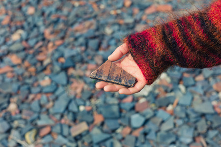 A womans hand is holding a piece of slate outside with gravel and rubble on the groundの写真素材