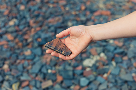 A womans hand is holding a piece of slate outside with gravel and rubble on the groundの写真素材