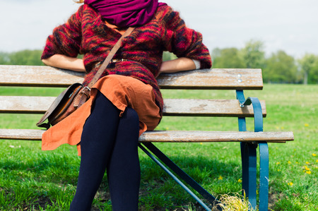 A young woman is sitting and resting on a bench outside in a parkの写真素材