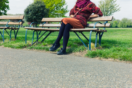 A young woman is sitting and resting on a bench outside in a parkの写真素材