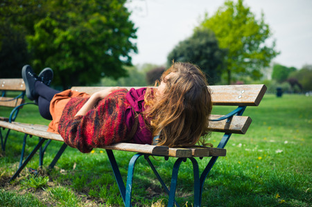 A young woman is lying on a bench and is relaxing in the park on a sunny spring dayの写真素材
