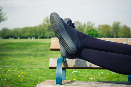 The legs of a young woman as she is lying on a bench in the park relaxingの写真素材