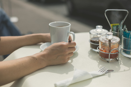 The hands of a woman resting on a table outside as she is drinking coffeeの写真素材