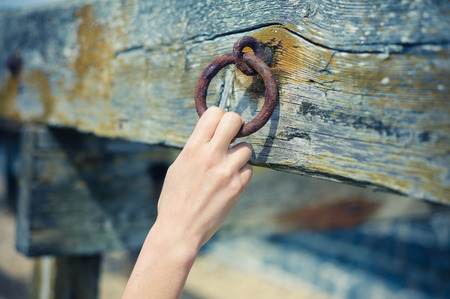 A young female hand is grabbing an old rusty chain attached to a wooden beamの写真素材