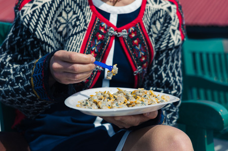 A young woman is eating cockles outside on a sunny dayの写真素材