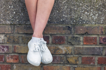 The legs of a young woman as she is sitting on a brick wall and is relaxing
