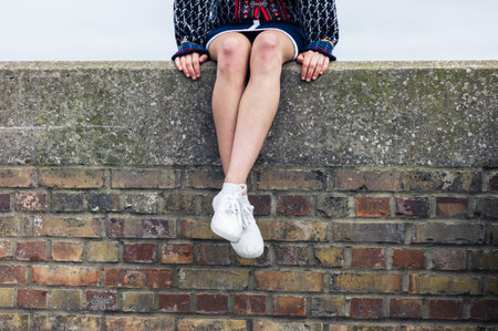 A young woman is sitting on a brick wall and is relaxing