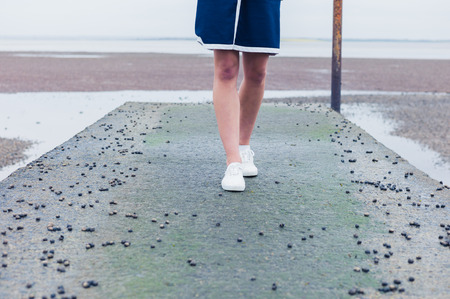 A young woman is walking on a pier by the sea covered in whelksの写真素材