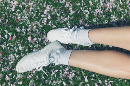 A young woman is lying on the green grass in a park covered with fallen cherry blossom on a sunny...