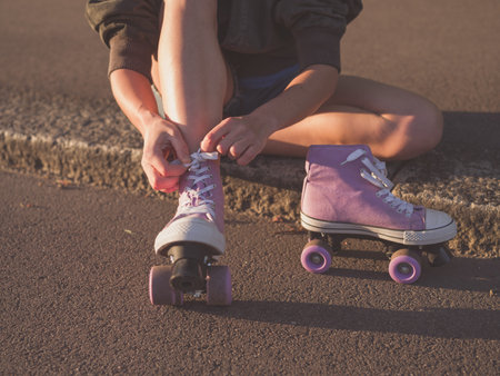 A young woman is sitting on the ground and is putting on roller skates in the park at sunset