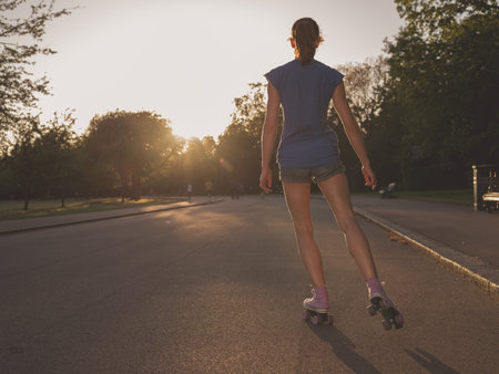 An attractive young woman is roller skating in a park at sunset