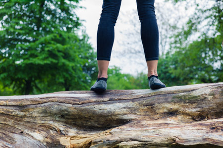 A young woman is standing on a tree trunk in a parkの写真素材