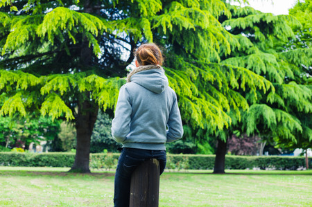 A young woman is sitting on a wooden post in the parkの写真素材