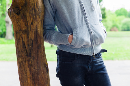 A young woman is leaning against a wooden post in the parkの写真素材