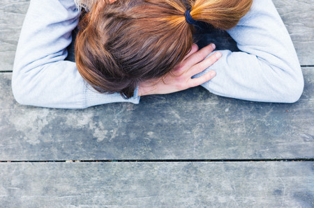 A sad young woman with her head resting on her hands at a table in the parkの写真素材