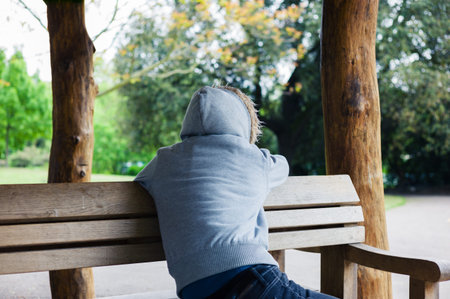 A young person wearing a hooded top is sitting in a shelter in the parkの写真素材