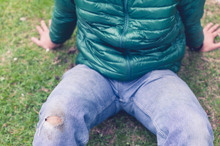 A trendy young man with a hole torn in his jeans at the knee is sitting on the grassの写真素材