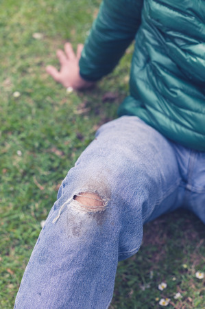A trendy young man with a hole torn in his jeans at the knee is sitting on the grassの写真素材