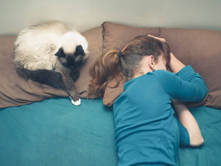 A young woman is sleeping in a bed with a cat next to herの写真素材