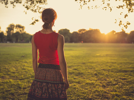 A young woman is standing in a park and is admiring the sunsetの写真素材