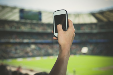 A female hand is holding a smart phone in a stadium to take pictures of a sporting eventの写真素材