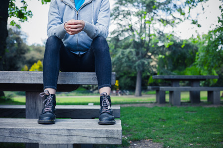 A young woman wearing boots is sitting on a bench in a parkの写真素材